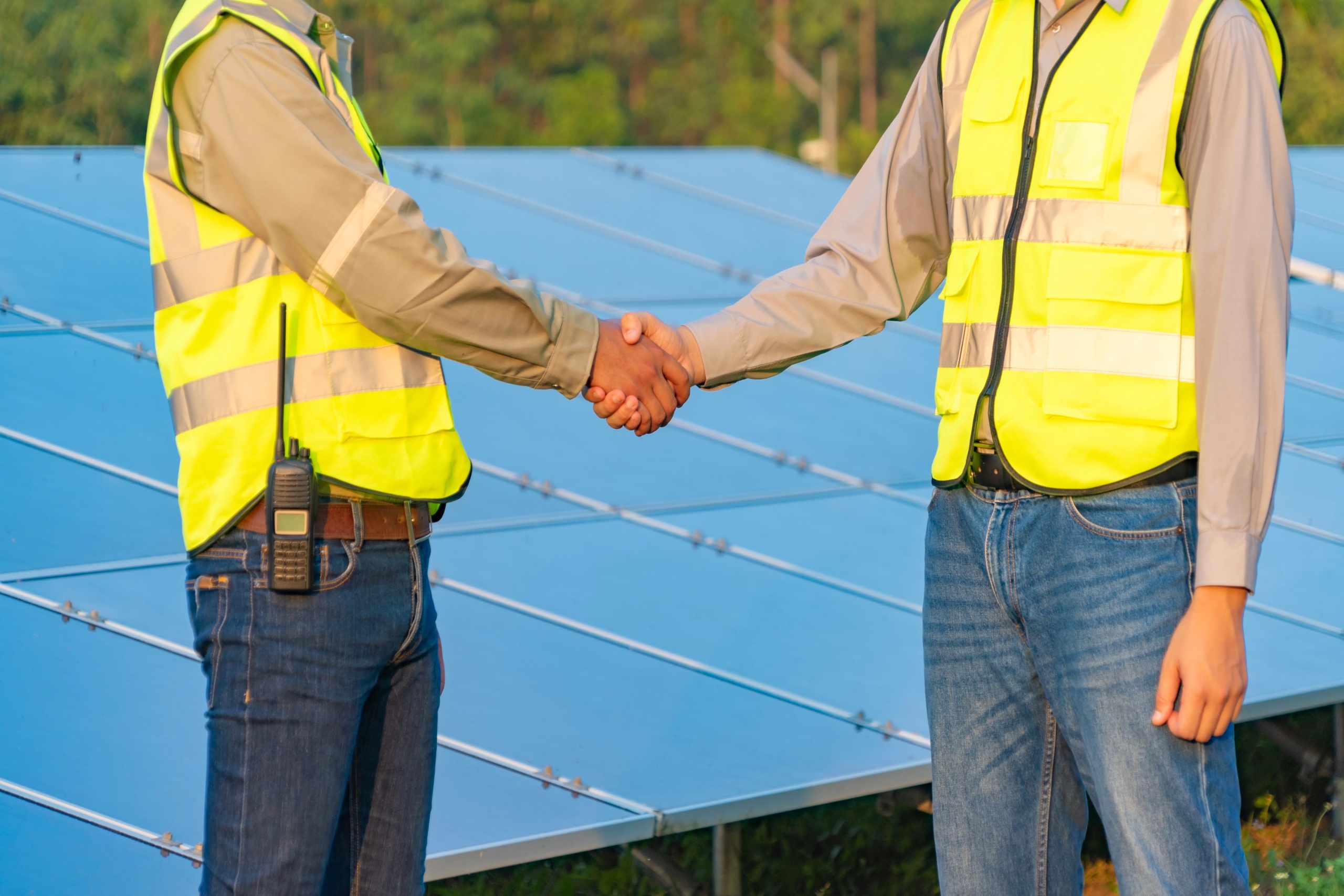 midsection men shaking hands by solar panel